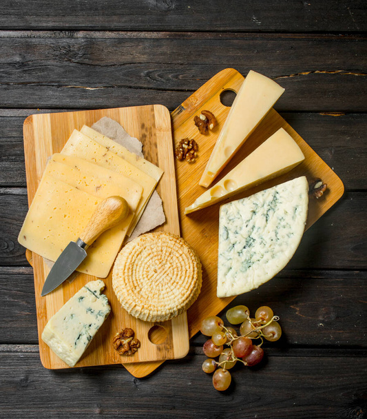 Assortment of different cheeses with grapes and walnuts. On a wooden background. - 写真・画像