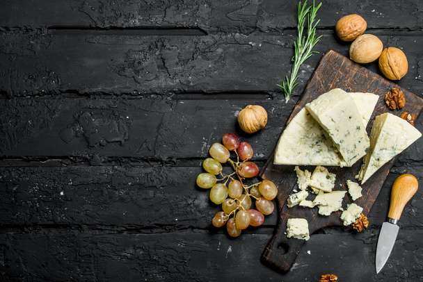 Blue cheese with grapes and rosemary. On a black rustic background. - Foto, immagini