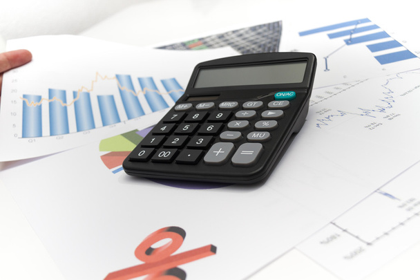 Бизнесмен анализирует инвестиционные графики с помощью калькулятора и лапта
 - Фото, изображение