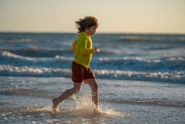 Excited kid running and playing on tropical beach in summer day. Kid enjoy outdoor activity. Summer vacation at the sea. Little boy running on beach at sunset. Kids on summer holiday vacation - Fotoğraf, Görsel