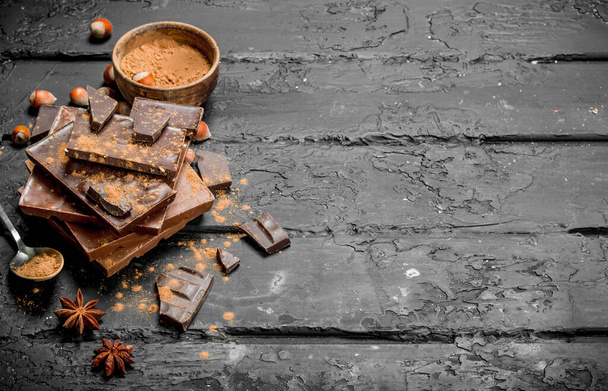 Assortment of different types of chocolate with cocoa powder. On black rustic background. - Foto, afbeelding