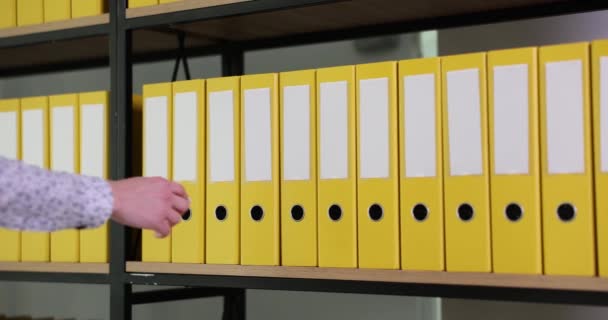 Женская рука берет жёлтую папку из офисного архива. Организованная структура папок и архив на большой стойке в современном офисном замедленном режиме - Кадры, видео