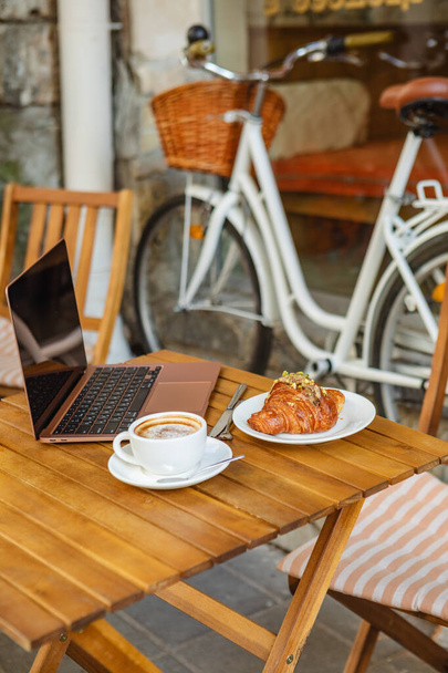 laptop, croissant, en koffie op cafes zomerterras - Foto, afbeelding