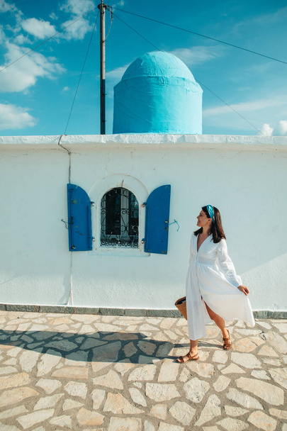piękna kobieta w białej sukience w pobliżu starego greckiego kościoła biały z niebieskim - Zdjęcie, obraz