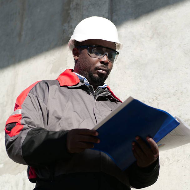 Afrikkalainen amerikkalainen työmies seisoo rakennustyömaalla ja näyttää työpapereita - Valokuva, kuva