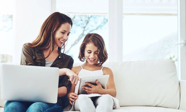 Technology, mother on laptop and helping daughter on tablet sitting on sofa in the living room of their home. Social media or connectivity, networking or streaming and woman with child happy on couch. - Foto, imagen