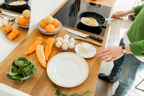 Gewassen uitzicht op de mens kookeitjes in de buurt van boter, paprika 's en spinazie op het werkblad in de moderne keuken - Foto, afbeelding