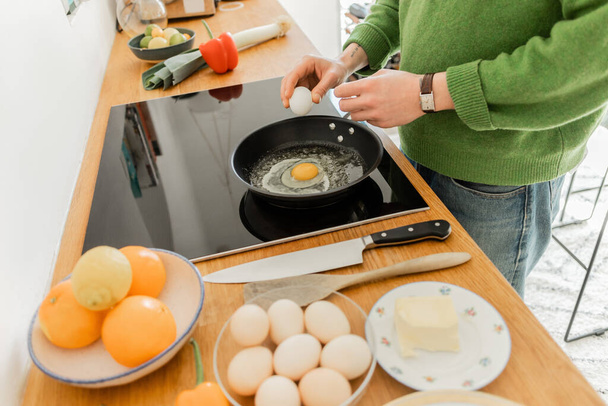Ausgeschnittene Ansicht tätowierter Mann mit Ei in der Nähe der Pfanne beim Kochen von Frühstück in der Nähe von Butter  - Foto, Bild