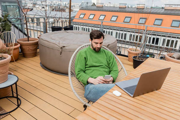 Bearded freelancer working near laptop on table on rooftop terrace of house in Vienna, Austria - Foto, Imagen