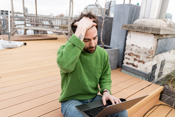 freelancer tocando el cabello y usando laptop en la terraza de la azotea en Viena, Austria - Foto, imagen