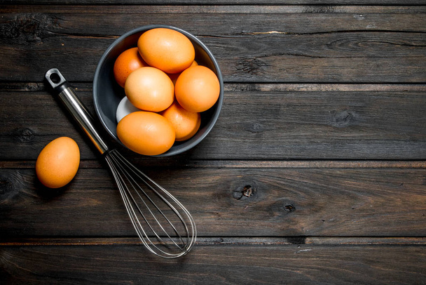 Eggs in a bowl with a whisk. On a wooden background. - Fotó, kép