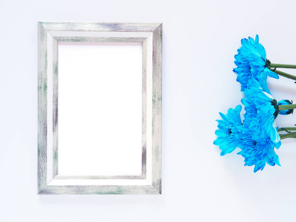 Grey rectangle border photo frame and blue flowers (chrysanthemum) on white background. Top view, flat lay with copy space - Fotografie, Obrázek