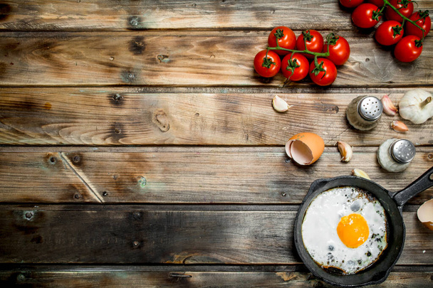 Fried egg in a pan with tomatoes. On a wooden background. - Fotografie, Obrázek
