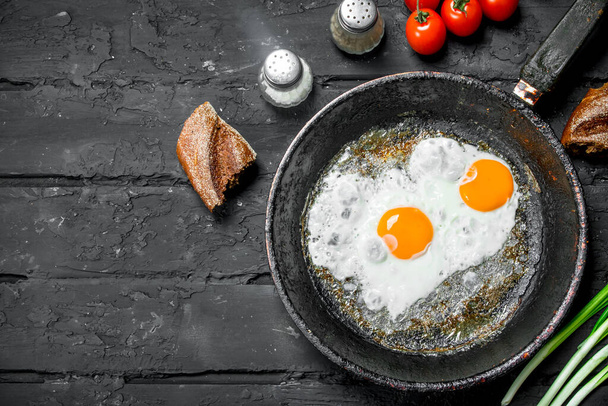 Fried eggs in a pan with bread and tomatoes. On black rustic background. - Φωτογραφία, εικόνα