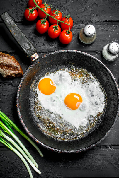 Fried eggs in a pan with bread and tomatoes. On black rustic background. - Foto, immagini
