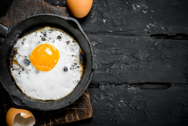 Fried egg in a frying pan. On black rustic background. - Фото, зображення