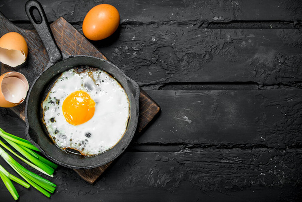 Fried egg with green onions and seasonings. On black rustic background. - Foto, Imagen