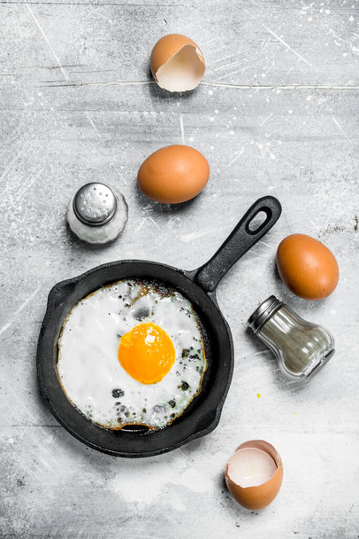 Fried egg with salt and black pepper. On a rustic background. - Photo, image