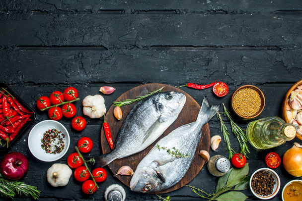 Raw sea fish dorado with spices and vegetables. On a black rustic background. - Фото, зображення