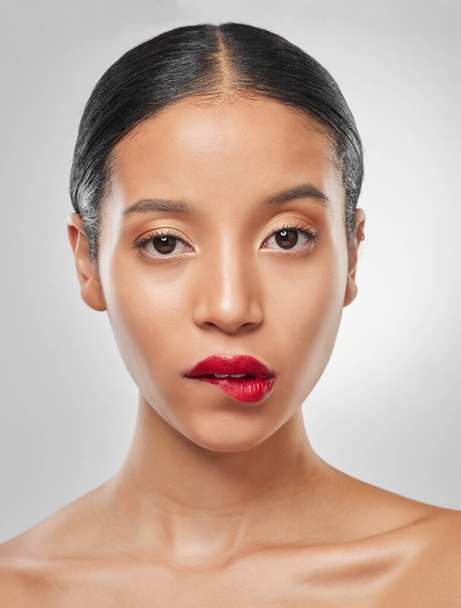 When a lipstick is so sexy it takes your breath away. Studio portrait of an attractive young woman wearing red lipstick and biting her lip against a grey background - Photo, Image