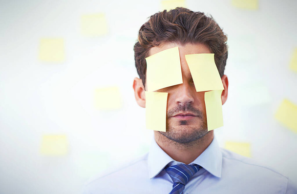 Feeling more than a little overwhelmed...a young businessman with sticky notes on his face - Foto, Bild