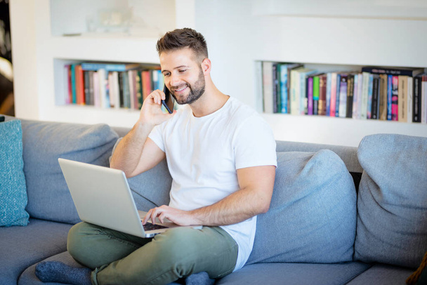 Handsome man using mobile phone and laptop for work at home. Home office. Confident businessman wearing casual clothes. - 写真・画像
