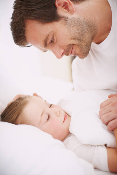 Her face looks so serene. Side view of a dad looking down lovingly at his sleeping daughter - Фото, изображение
