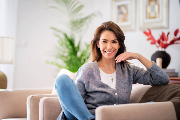 Portrait of beautiful long haired woman wearing casual clothes while relaxing in an armchair at home.  - Foto, Imagem