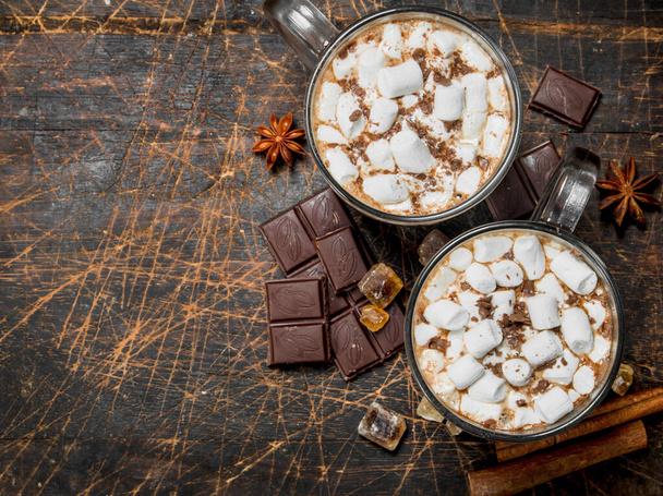 Hot chocolate in mugs with marshmallows and fragrant cinnamon. On a wooden background. - Zdjęcie, obraz