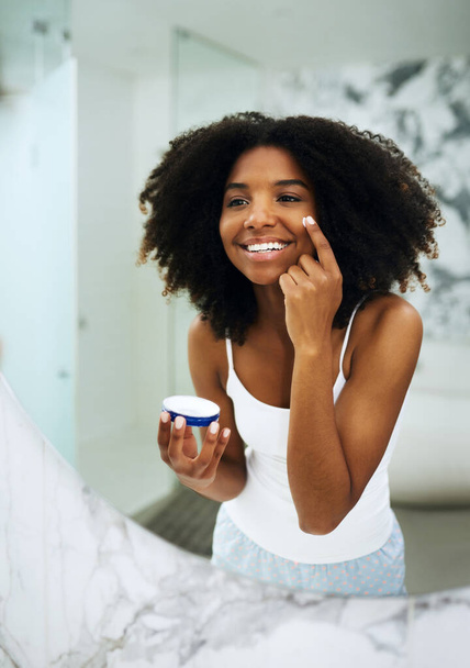 Skin care, happiness and black woman in bathroom mirror with cream, smile and morning dermatology routine. Health, wellness and luxury skincare at home, girl in reflection and lotion on face for glow. - Foto, Bild