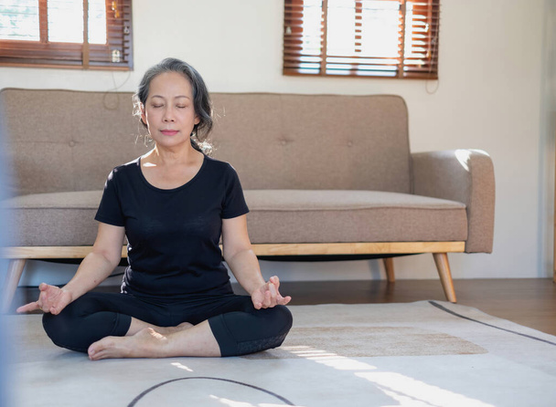 Aasialainen iäkäs nainen meditoi joogaa hyvää terveyttä varten Vanhemmassa iässä kyse on kehon terveydestä huolehtimisesta kotona rentouttavana päivänä. hyvä terveyden käsite - Valokuva, kuva