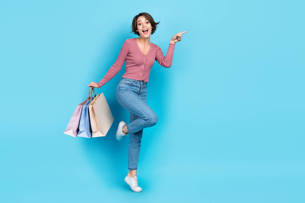Full body photo of astonished funky lady hold mall bags direct finger empty space isolated on blue color background. - Valokuva, kuva