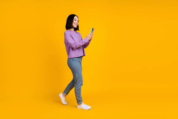 Full body size photo of young chinese blogger girl hold phone walking recording video online popularity isolated on yellow color background. - Fotó, kép