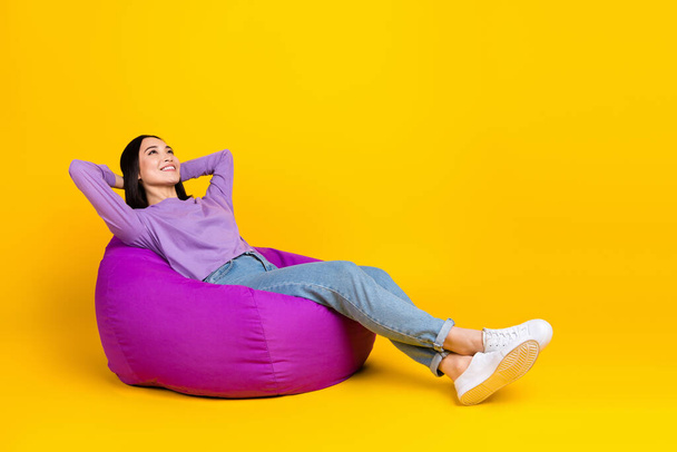 Full body photo of young chinese girl wear purple shirt denim jeans take nap rest hands head bean bag isolated on yellow color background. - Foto, Imagem