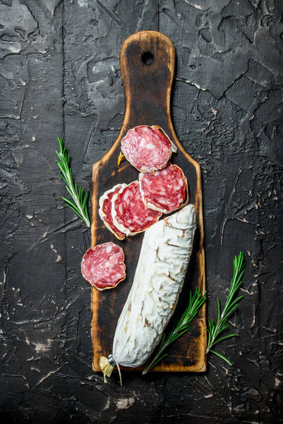 Salami with fragrant rosemary. On black rustic background. - Foto, imagen