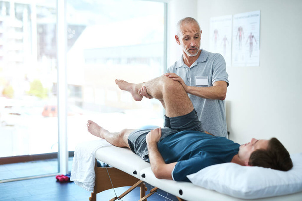 Physical therapist, client and man with leg injury, healing and consultation for rehabilitation. Male person, customer and chiropractor with physiotherapist, healthcare and wellness with stretching. - Photo, Image