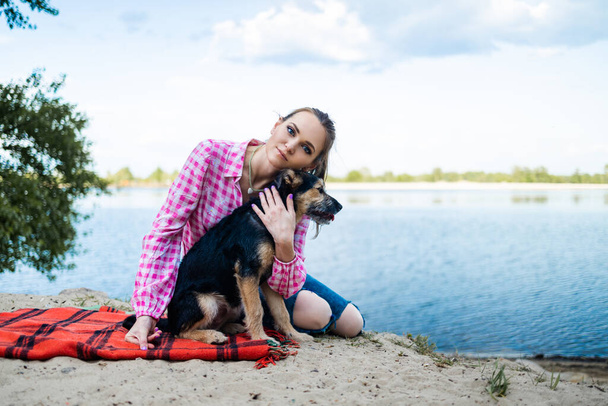 vrouw die plezier heeft met hond in het park, zittend op deken in de zomer. Een knuffelende vrouw. Huisdieren en liefde concept. - Foto, afbeelding