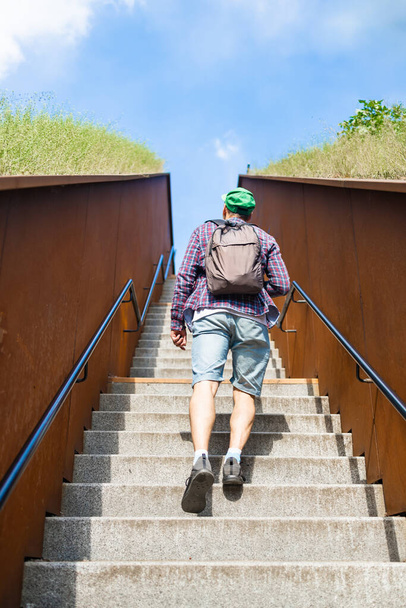 Visszapillantás fiatalember utazik hátizsák megy fel a lépcsőn egy napsütéses napon. Kilátások hátulról és alulról. - Fotó, kép