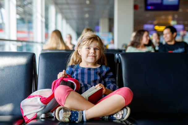 大きな窓から搭乗を待っている空港の少女。かわいい子供がパスポートを持っています家族の夏休みに出発するのを楽しみにしています. - 写真・画像
