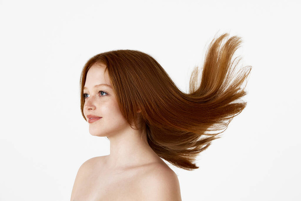 Side view portrait of young beautiful redhead girl with well-kept straight hair posing against white studio background. Concept of natural beauty, hair cosmetics, treatment, cosmetology, skin care - Foto, imagen