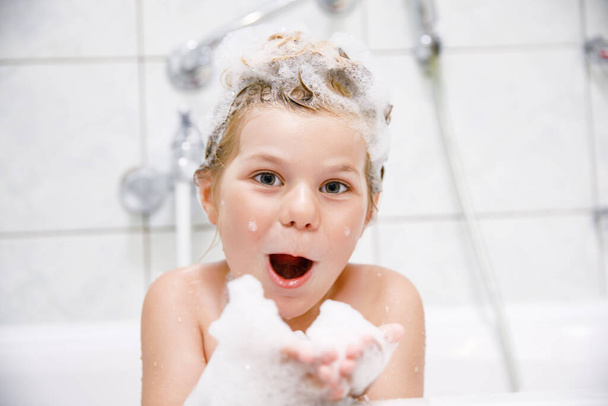 Cute child with shampoo foam and bubbles on hair taking bath. Portrait of happy smiling preschool girl health care and hygiene concept. Washes hair by herself - Foto, Bild