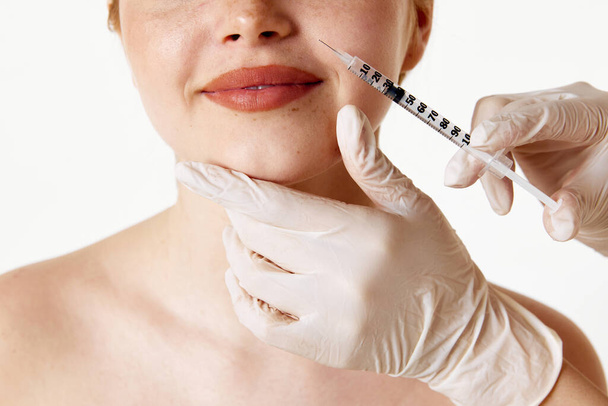 Anti-wrinkles care. Cropped image of female face with syringe making beauty filler injection against white studio background. Concept of beauty, plastic surgery, cosmetology, cosmetics, skin care - Foto, Bild