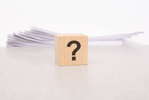 ein Holzblock mit einem Fragezeichen auf einem Stapel von Dokumenten. grauer Tisch, weißer Hintergrund - Foto, Bild