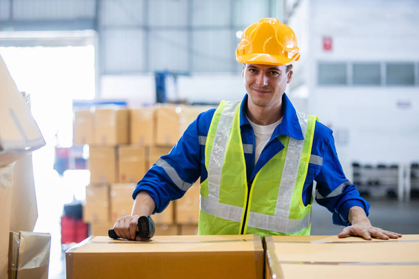 Man professional worker wearing safety uniform and hard hat worker package box product on shelves in warehouse. Male worker storehouse logistic storage product. - Photo, Image