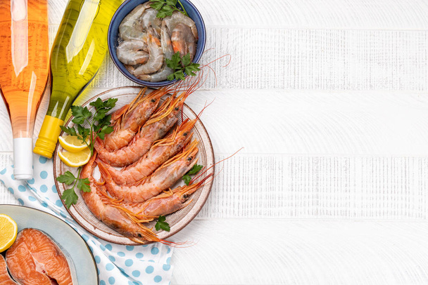 A top view photo of fresh seafood such as shrimp, lobster, and trout steaks, accompanied by white and rose wine. Flat lay with copy space - 写真・画像