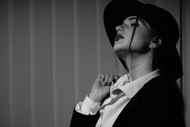 Stüdyoda poz veren siyah ceketli ve şapkalı güzel bir genç kızın siyah beyaz fotoğrafı. - Fotoğraf, Görsel