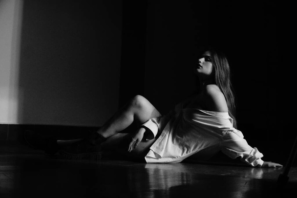 черно-белое фото красивой молодой девушки в одной белой рубашке над ее обнаженным телом, позирующей в студии - Фото, изображение