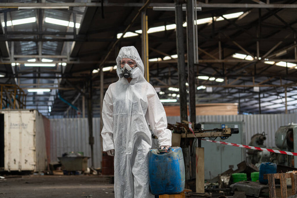PPE koruyucu giysiler ve gaz maskeleri takan beyaz kadın işçiler, ellerinde eski benzin tankları tutuyorlardı.. - Fotoğraf, Görsel