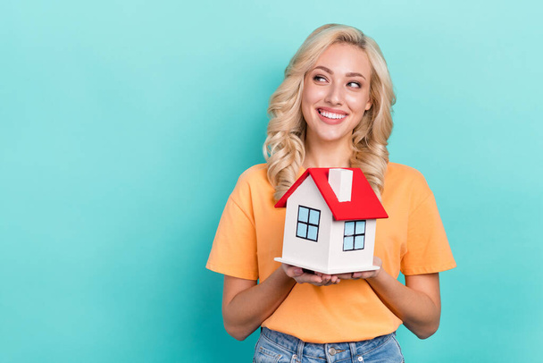 Photo of dreamy funny lady dressed orange t-shirt looking empty space showing little house isolated teal color background. - Foto, Imagem