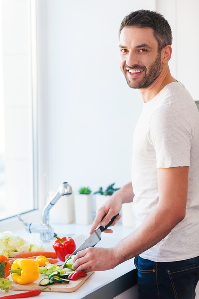 Young man cutting vegetables and smiling - Fotó, kép